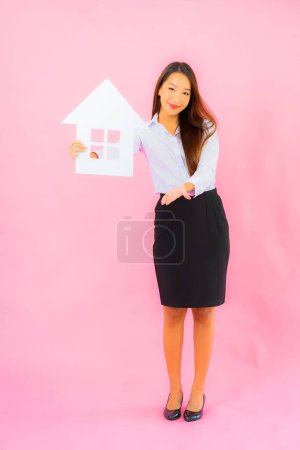 Téléchargez les photos : Portrait belle jeune femme asiatique montrer maison ou signe de maison sur fond de couleur rose - en image libre de droit