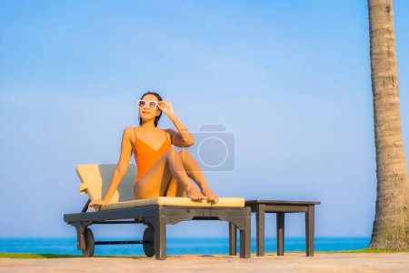 Téléchargez les photos : Portrait belle jeune femme asiatique relax sourire loisirs autour de la piscine extérieure avec vue sur la mer océan - en image libre de droit