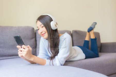 Photo for Portrait beautiful young asian woman use smart mobile phone headphone for listen music in living room - Royalty Free Image