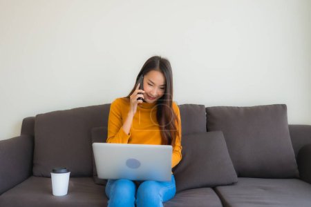 Téléchargez les photos : Portrait jeune femme asiatique en utilisant ordinateur portable carnet de notes avec téléphone portable intelligent et tasse de café - en image libre de droit