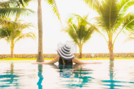 Foto de Retrato hermosa mujer asiática joven relajarse alrededor de la piscina al aire libre en el complejo hotelero con palmera al atardecer o al amanecer para vacaciones de ocio - Imagen libre de derechos