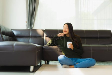 Téléchargez les photos : Portrait belle jeune femme asiatique utiliser téléphone portable intelligent avec tasse de café avec canapé dans le salon intérieur - en image libre de droit