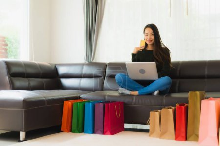Foto de Retrato hermosa mujer asiática joven uso portátil y tarjeta de crédito con bolsa de compras para las compras en línea en casa - Imagen libre de derechos