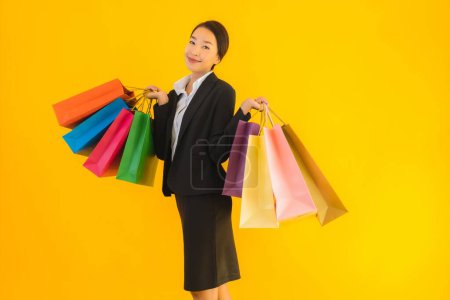Téléchargez les photos : Portrait belle jeune femme asiatique d'affaires avec sac à provisions de centre commercial sur fond jaune isolé - en image libre de droit