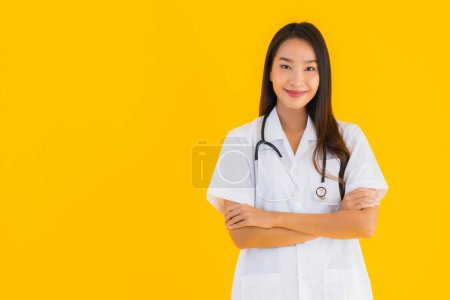 Téléchargez les photos : Portrait belle jeune asiatique médecin femme sourire heureux travail à l'hôpital et clinique sur fond jaune isolé - en image libre de droit