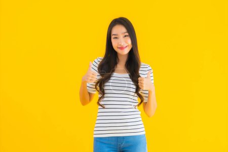 Téléchargez les photos : Portrait belle jeune femme asiatique sourire heureux avec action sur fond jaune isolé - en image libre de droit