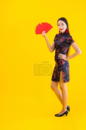 Téléchargez les photos : Portrait belle jeune femme asiatique porter robe chinoise avec Ang Pao ou lettre rouge avec de l'argent pour la nouvelle année chinoise concept sur fond isolé jaune - en image libre de droit