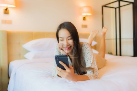 Foto de Retrato hermosa joven mujer asiática en la cama con teléfono móvil inteligente en el interior del dormitorio - Imagen libre de derechos
