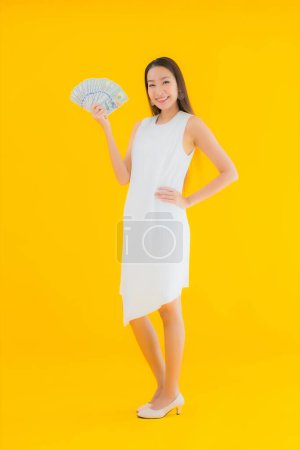 Foto de Retrato hermosa joven asiática mujer con dinero en efectivo en amarillo aislado fondo - Imagen libre de derechos