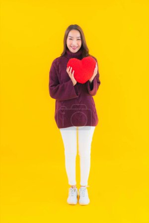 Téléchargez les photos : Portrait belle jeune femme asiatique avec forme d'oreiller de coeur sur fond jaune isolé - en image libre de droit
