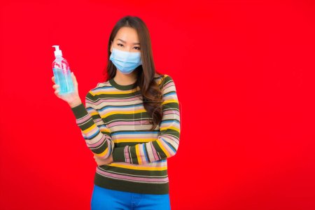 Téléchargez les photos : Portrait belle jeune femme asiatique avec gel d'alcool sur fond rouge isolé - en image libre de droit