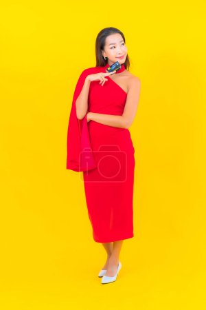 Téléchargez les photos : Portrait belle jeune femme asiatique avec carte de crédit sur fond jaune - en image libre de droit