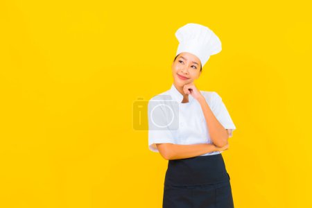 Photo for Portrait beautiful young asian woman in chef or cook uniform with hat on yellow isolated background - Royalty Free Image