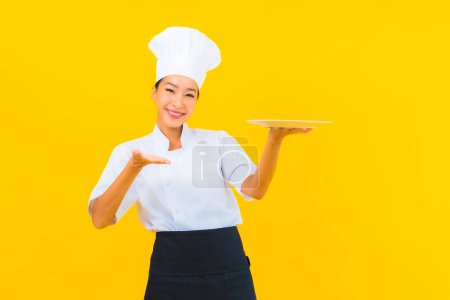 Photo for Portrait beautiful young asian chef woman with plate on yellow isolated background - Royalty Free Image