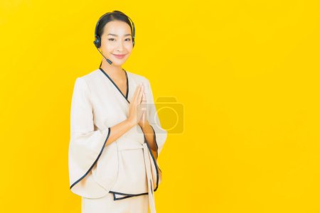 Téléchargez les photos : Portrait belle jeune femme asiatique d'affaires avec casque pour le service à la clientèle du centre d'appels sur fond jaune - en image libre de droit