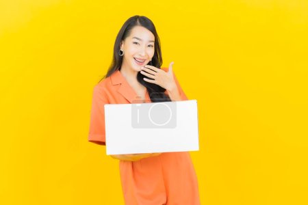 Téléchargez les photos : Portrait belle jeune femme asiatique avec boîte prête pour l'expédition sur fond de couleur jaune - en image libre de droit
