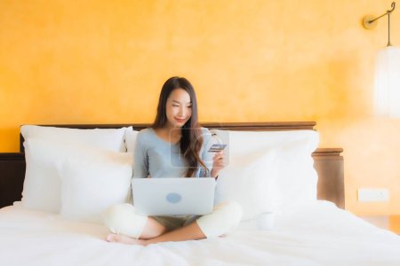 Photo for Portrait beautiful young asian woman using computer notebook or laptop with credit card on bed in bedroom interior - Royalty Free Image