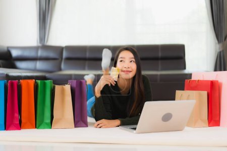 Foto de Retrato hermosa mujer asiática joven con bolsa de compras y tarjeta de crédito con teléfono móvil para las compras en línea en casa - Imagen libre de derechos