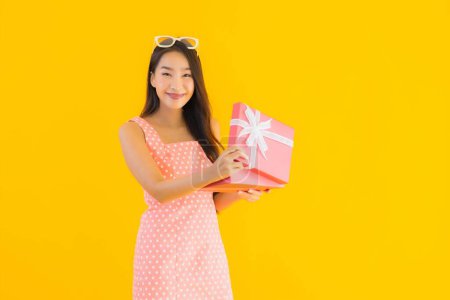 Téléchargez les photos : Portrait belle jeune femme asiatique avec boîte cadeau rouge sur fond jaune isolé - en image libre de droit