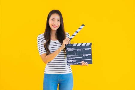 Photo for Portrait beautiful young asian woman show clapper movie board on yellow isolated background - Royalty Free Image