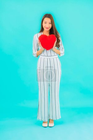 Téléchargez les photos : Portrait belle jeune femme asiatique avec forme d'oreiller de coeur sur fond bleu - en image libre de droit