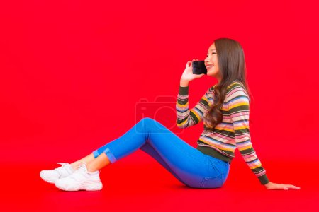 Téléchargez les photos : Portrait belle jeune femme asiatique utiliser téléphone mobile intelligent sur fond rouge isolé - en image libre de droit