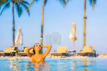 Foto de Retrato hermosa joven mujer asiática relajarse sonrisa ocio alrededor de piscina al aire libre con vista al mar océano - Imagen libre de derechos