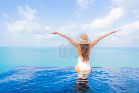 Foto de Retrato hermosa joven mujer asiática relajarse sonrisa ocio alrededor de piscina al aire libre con mar océano en vacaciones de viaje - Imagen libre de derechos
