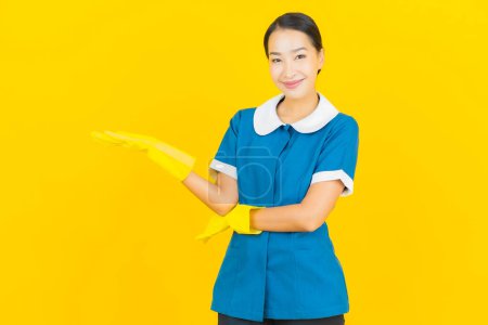 Foto de Retrato hermosa joven asiática mujer mucama y limpieza sonrisa con acción en color amarillo fondo - Imagen libre de derechos