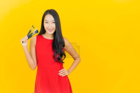 Téléchargez les photos : Portrait belle jeune femme asiatique avec pinceau cosmétique sur fond jaune - en image libre de droit