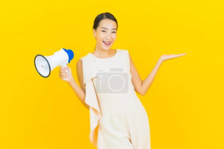 Téléchargez les photos : Portrait belle jeune femme asiatique sourire avec mégaphone sur fond de couleur jaune - en image libre de droit
