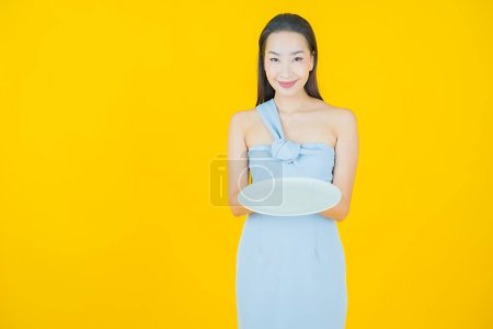 Téléchargez les photos : Portrait belle jeune femme asiatique sourire avec plat vide sur fond de couleur - en image libre de droit