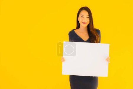 Photo for Portrait beautiful young asian woman with empty and blank billboard card banner on yellow isolated background - Royalty Free Image