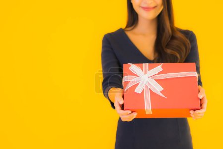 Téléchargez les photos : Portrait belle jeune femme asiatique avec boîte cadeau sur fond jaune isolé - en image libre de droit