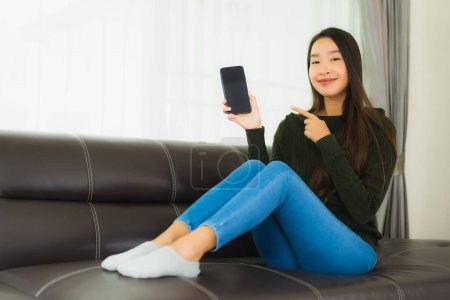 Téléchargez les photos : Portrait belle jeune femme asiatique utiliser téléphone mobile intelligent ou téléphone portable sur canapé dans le salon intérieur - en image libre de droit