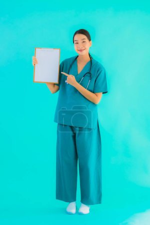 Téléchargez les photos : Portrait belle jeune femme asiatique médecin avec carton vide pour l'espace de copie sur fond bleu isolé - Soins de santé à l'hôpital et concept de clinique - en image libre de droit