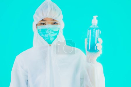 Photo for Portrait beautiful young asian doctor woman wear ppe suite and mask with alcohol gel on blue isolated background - Royalty Free Image