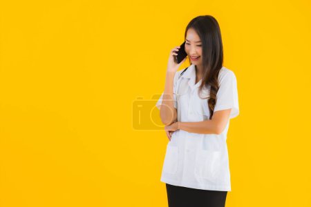 Photo for Portrait beautiful young asian doctor woman use smart mobile cell phone on yellow isolated background - Royalty Free Image