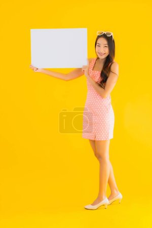 Téléchargez les photos : Portrait belle jeune asiatique femme montrer vide panneau d'affichage blanc pour texte et copyspace sur fond jaune isolé - en image libre de droit