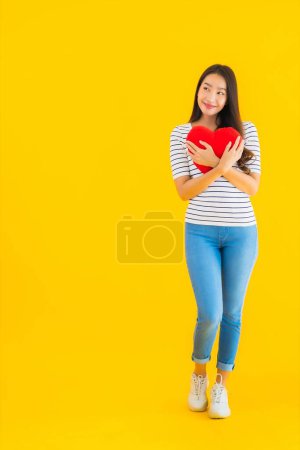 Téléchargez les photos : Portrait belle jeune femme asiatique montrer oreiller coeur sur fond jaune isolé - en image libre de droit