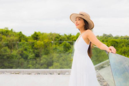 Téléchargez les photos : Portriat belle jeune femme asiatique sourire heureux autour du balcon avec vue sur la mer arrière-plan - en image libre de droit