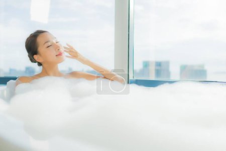 Téléchargez les photos : Portrait belle jeune femme asiatique se détendre profiter dans la baignoire dans la salle de bain intérieure - en image libre de droit