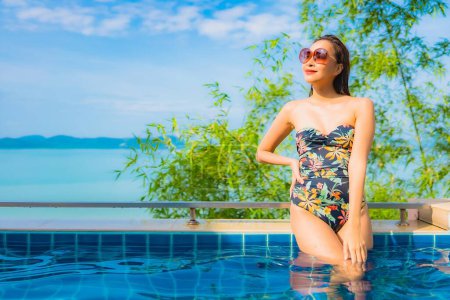 Foto de Retrato hermosa joven mujer asiática relajarse sonrisa ocio alrededor de piscina al aire libre con vista al mar océano para vacaciones de viaje - Imagen libre de derechos