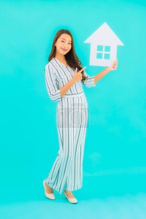Téléchargez les photos : Portrait belle jeune femme asiatique montrer la maison ou signe de maison sur fond bleu - en image libre de droit