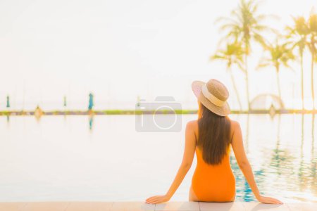 Téléchargez les photos : Portrait belle jeune femme asiatique relax sourire loisirs autour de la piscine extérieure presque mer plage océan au coucher du soleil temps des vacances - en image libre de droit