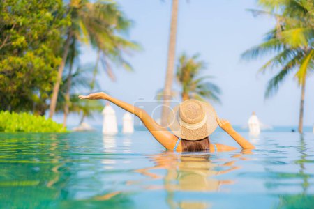 Foto de Retrato hermosa joven mujer asiática relajarse sonrisa disfrutar de ocio alrededor de la piscina casi mar playa vista al mar para vacaciones de ocio - Imagen libre de derechos