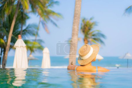 Foto de Retrato hermosa joven mujer asiática relajarse sonrisa disfrutar de ocio alrededor de la piscina casi mar playa vista al mar para vacaciones de ocio - Imagen libre de derechos