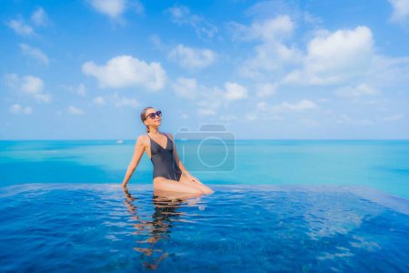 Foto de Retrato hermosa joven mujer asiática relajarse sonrisa ocio alrededor de la piscina al aire libre en resort hotel con vista al mar océano - Imagen libre de derechos