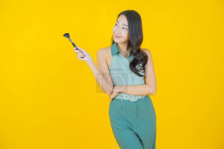 Foto de Retrato hermosa joven asiática mujer con maquillaje cepillo cosmético en color de fondo - Imagen libre de derechos