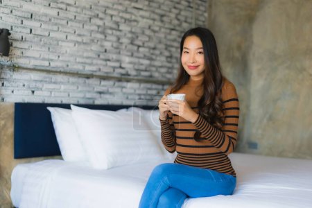 Téléchargez les photos : Jeune femme asiatique avec tasse de café sur le lit dans la chambre intérieure - en image libre de droit